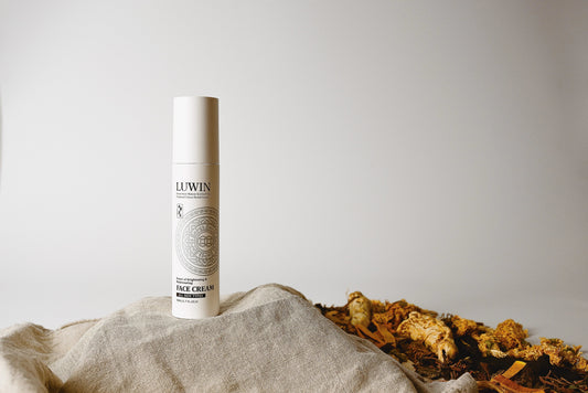 LUWIN traditional Chinese herbal face cream bottle displayed on a neutral textured linen cloth next to dried botanicals and medicinal roots.