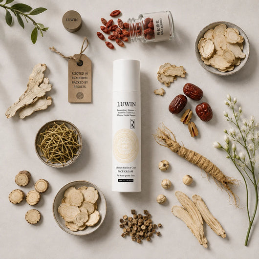 A white cylindrical bottle of LUWIN Face Cream is centered in a styled flat-lay arrangement with Chinese herbal ingredients including sliced roots, red dates, dried flowers, and bark on a light neutral background.