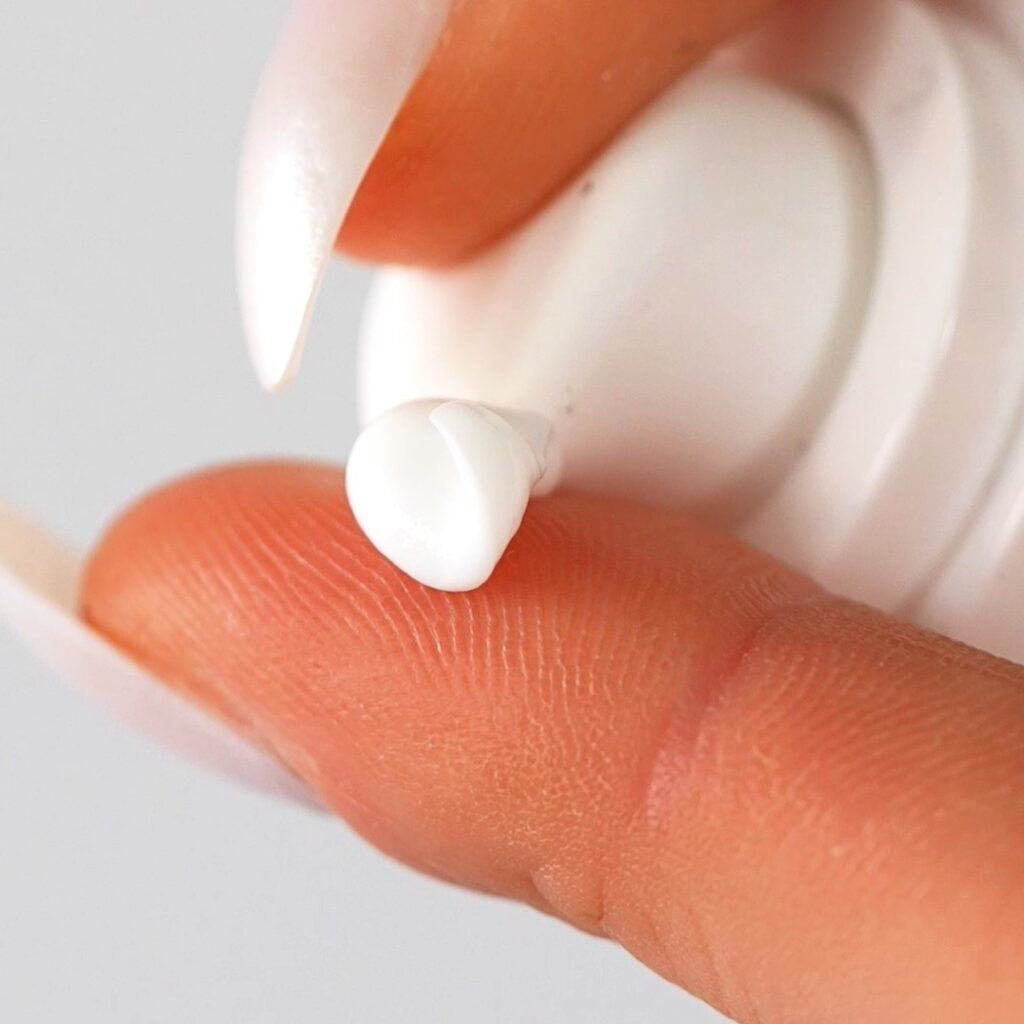 Close-up images of a luxurious white cream with a smooth, velvety texture, carefully dispensed onto fingertips, highlighting the cream’s rich yet lightweight consistency for targeted brightening and rejuvenation.